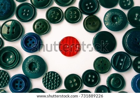  Around the red button is a background of dark buttons of different sizes. Confrontation of the individual and the hostile world. Loneliness among people. Difference from the others.