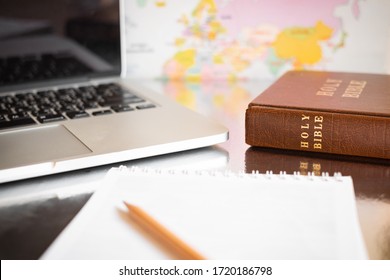 Around The World Learning Or Studying Bible Via Online By Using Laptop With Background Of World Map And Foreground Of Notebook.