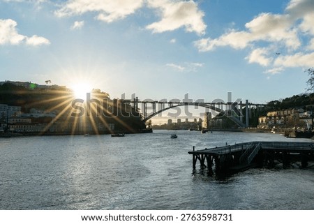 Arrabida bridge over Douro river in Porto Portugal at sunset with sun rays and city waterfront. Scenic urban landscape with boats, river reflections and warm evening light.