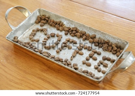 arrange coffee beans to make the word coffee in a stainless tray on a wooden table
