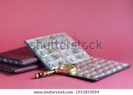 Сoins are arranged in transparent blisters on pink background. Page from album full with old coins. Magnifying glass is placed on blisters. Coin storage method. Numismatic collection in albums.