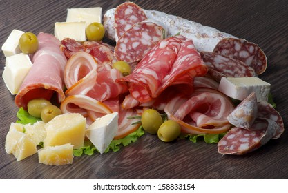 Arrangement of Delicatessen Cold Cuts with Smoked Ham, Pepperoni, Salami, Finocchiona, Green Olives, Grana Padano and Camembert Cheese closeup on Dark Wooden background