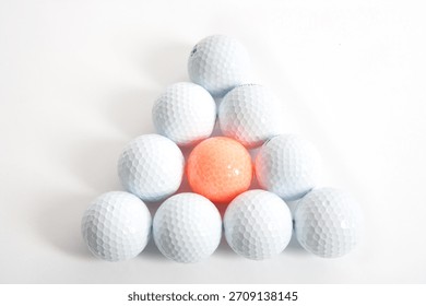 Arrangement of golf balls in a triangular shape with one orange ball at the center on a white background