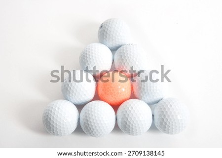 Arrangement of golf balls in a triangular shape with one orange ball at the center on a white background