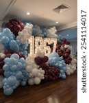 An arrangement of large marquee numbers displaying “1867,” surrounded by clusters of burgundy, blue, and white balloons, creating a festive and elegant backdrop for a sorority celebration.