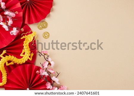 Arranging an exquisite Chinese New Year décor arrangement. Top view shot of red folding fans, sakura, gold dragon, lanterns, gold coins, on beige background with advert spot