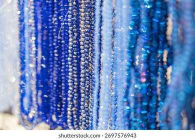 Array of blue gemstone beads, varying sizes and intensities, hanging downward from white strings on a gray surface, casting subtle shadows Soft lighting, multiple layers of beads in the background,