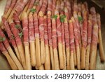 An array of breadsticks wrapped in bacon with a garnish of green leaves