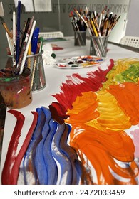 An array of colorful paint strokes on a white surface with multiple artist brushes and art supplies in the background