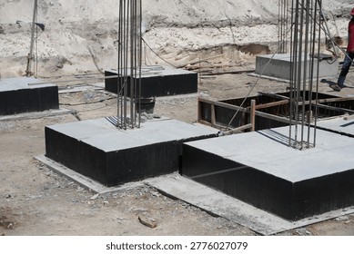 An array of concrete footings, each with embedded rebar columns, are shown prepared for the next phase of construction, with a person visible in the background.