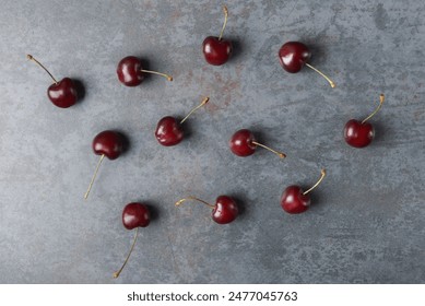 An array of dark red cherries with stems, freshly picked and scattered on a grey textured backdrop, highlighting the fruit’s natural gloss and rich color - Powered by Shutterstock