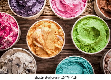 Array of different flavored colorful ice cream in plastic tubs displayed on an old wooden table at an ice cream parlor for delicious frozen snacks on a hot summer day