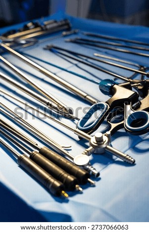 Array of laparoscopic instruments and medical devices on sterile table. Perspective view of long surgical shafts and handles on a blue surgical drape.