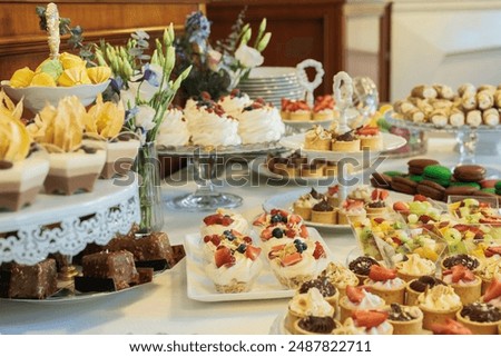 An array of sweet treats, including mini tarts, pastries, and cakes, adorn a white table adorned with delicate floral arrangements, creating a delightful scene for a special event