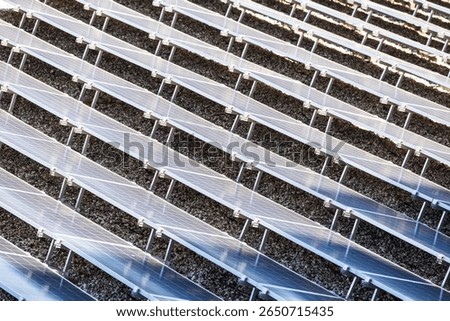 An array of tilted solar panels arranged in precise rows on a gravel-covered surface, capturing sunlight for renewable energy production