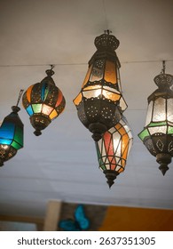 An array of vibrant, ornate Moroccan lanterns with stained glass hang from a ceiling, casting a warm and inviting glow