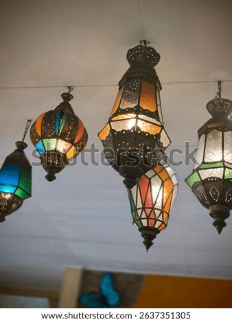 An array of vibrant, ornate Moroccan lanterns with stained glass hang from a ceiling, casting a warm and inviting glow