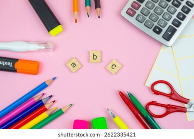 An array of vibrant school supplies is thoughtfully arranged around colorful ABC letters on a playful pink backdrop