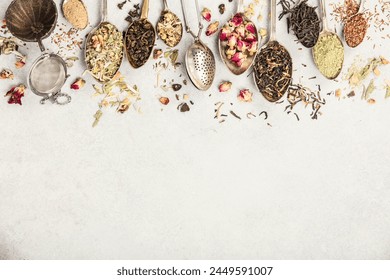 An array of vintage spoons, each containing different types of loose-leaf tea, laid out on a neutral backdrop. The selection showcases a variety of flavors and colors
