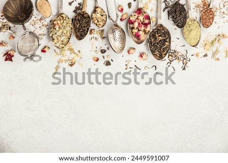 An array of vintage spoons, each containing different types of loose-leaf tea, laid out on a neutral backdrop. The selection showcases a variety of flavors and colors