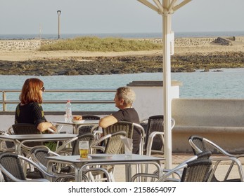 ARRECIFE, SPAIN - Feb 27, 2022: A Couple Of Women Sitting Having A Drink On A Terrace Overlooking The Sea In Lanzarote, Canary Islands