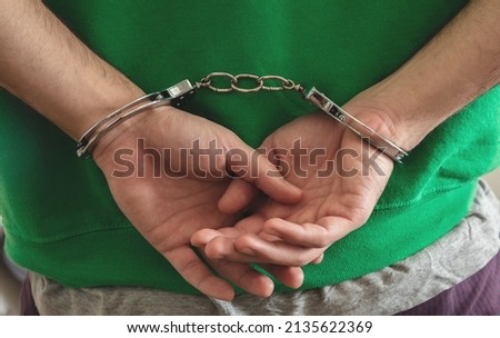 Arrest, Handcuffed criminal man hands close up. Hand cuffs locked behind. Crime and law violation concept. 