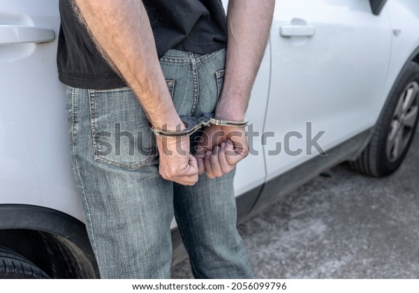 ARRESTED AND HANDCUFFED MAN ON THE STREET NEXT TO A\
CAR. REAR VIEW.