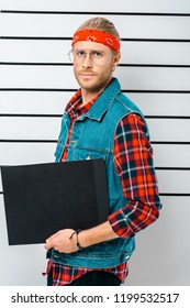 Arrested Hipster Man In Eyeglasses And Headband Holding Empty Prison Board In Front Of Police Line Up