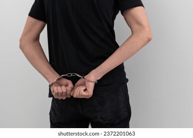 arrested man with cuffed hands behind prison bars.