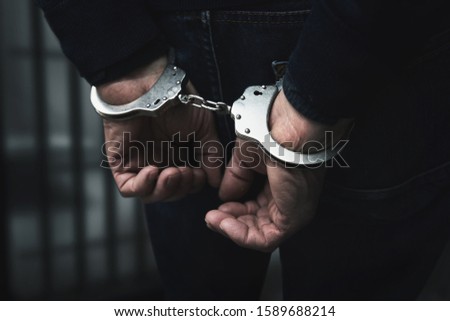 arrested man with cuffed hands behind prison bars