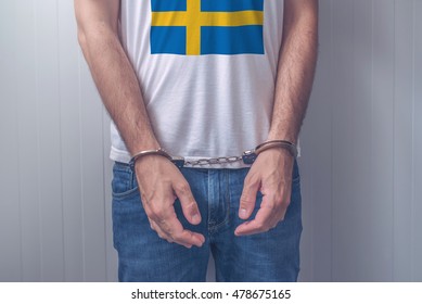 Arrested Man With Cuffed Hands Wearing Shirt With Swedish Flag. Unrecognizable Male Person In Jeans With Handcuffs Held In Police Station For Being Suspected Of A Crime.