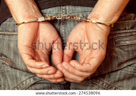 Arrested man handcuffed hands at the back. Closeup