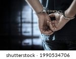 Arrested man in handcuffs with handcuffed hands behind back in prison
