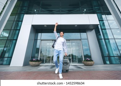 Arriving At Airport. Young Man Greeting Friends, Walking With Suitcase