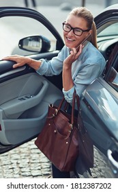 Arriving At Work In The Morning. Fashionable Middle Aged Business Woman With Handbag Getting Out Of Her Car, She Is Talking On Phone And Smiling