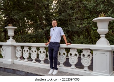 An arrogant rich young guy poses for a camera in the park with a smile. Successful businessman poses in the park at the parapet. - Shutterstock ID 2252594005