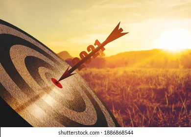 An Arrow With 2021 Numbers Is Inserted Into The Target Board Against The Background Of The Orange Nature Of The Morning Sun. Concept Form 2020 Year To New Year 2021 Vision. 