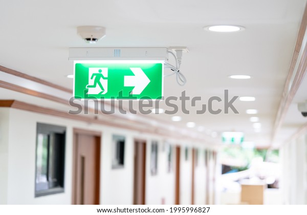 A Arrow light box sign of EMERGENCY FIRE EXIT is\
hung on the ceiling in hospital walkway, Idea for event fire or\
evacuation drills.