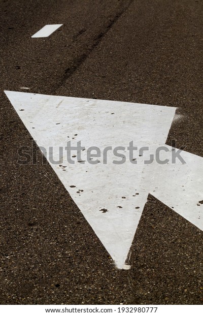 arrow on the asphalt to regulate the traffic of\
cars, close-up of the arrow part of the white color on the asphalt\
of the black dark color
