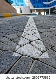 Arrow painted on cobblestone path leads toward modern building. Urban setting with blue glass facade