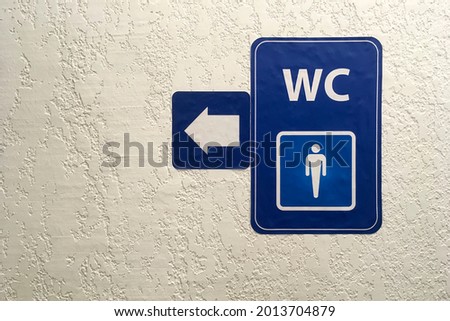 Arrow, pointer on blue plate of public male toilet signÐ± on plastered wall. Toilet sign. Restroom Concept .WC. Horizontal shot. Copy space. Close-up. Indoors.