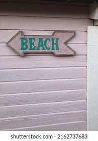 Arrow Shaped Wooden Beach Sign On Pink Beach Hut. 