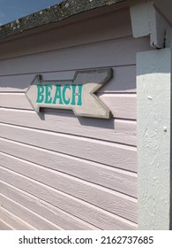 Arrow Shaped Wooden Beach Sign On Pink Beach Hut. 