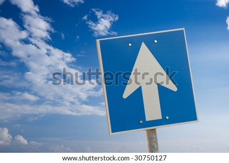 Arrow sign against bright blue sky with white clouds
