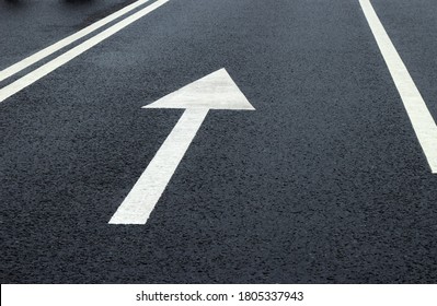 Arrow Sign On The Road. White Arrow On The Asphalt. White Forward Arrow On A Blurry Street Background