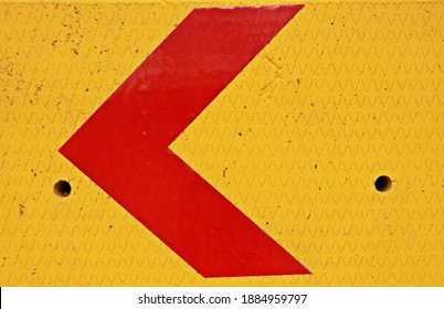 Arrow Sign Painted In Red On Yellow Wall. Concrete Traffic Barrier With Left Arrow Sign On It

