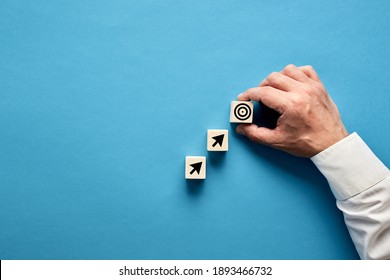 Arrow and target symbols on wooden blocks with a businessman hand placing the target symbol. Goal or agenda setting in business concept. - Shutterstock ID 1893466732