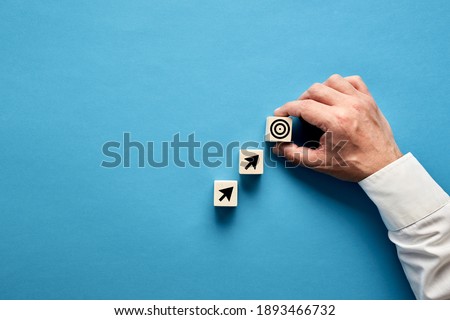 Arrow and target symbols on wooden blocks with a businessman hand placing the target symbol. Goal or agenda setting in business concept.
