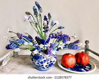 The art of arranging bouquets of flowers. Romantic bouquet in a decorative vase on a coffee table with pomegranate fruits. In composition - muscari and other primroses