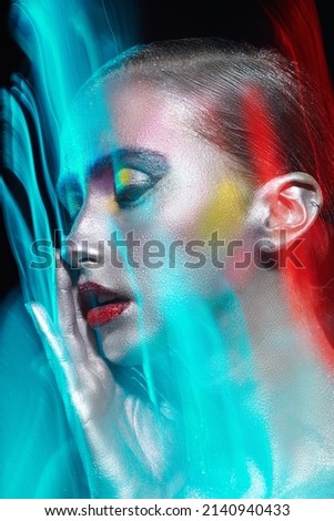 Art, beauty and fashion. Studio portrait of a girl with painted sparkling silvery skin on a black background in multicoloured light with dynamic blurs. Glitter makeup, body painting.